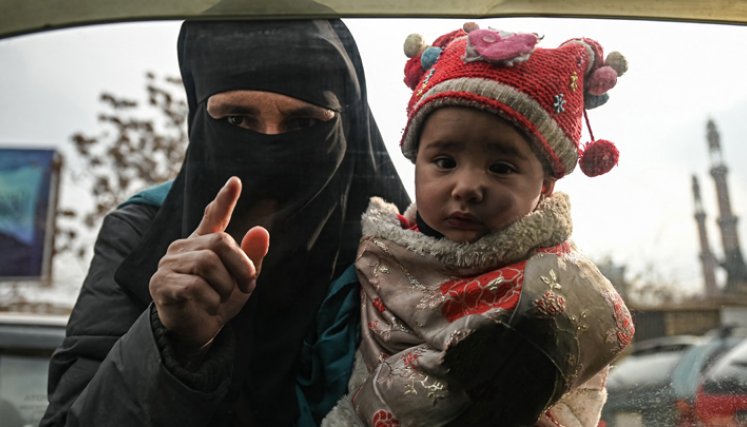 Una mujer carga a un niño mientras suplica a los viajeros en un automóvil en Kabul, el 26 de diciembre de 2021. / Foto:AFP