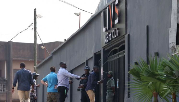 Transeúntes pasan junto a los policías que hacen guardia en la entrada del club nocturno Livs, donde se produjo un incendio mortal en el distrito de Bastos de Yaundé. / Foto: AFP
