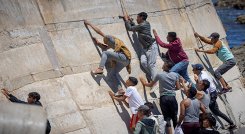 Migrantes escalan un malecón en la ciudad norteña de Fnideq después de intentar cruzar la frontera de Marruecos al enclave español de Ceuta.