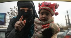 Una mujer carga a un niño mientras suplica a los viajeros en un automóvil en Kabul, el 26 de diciembre de 2021. / Foto:AFP