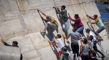 Migrantes escalan un malecón en la ciudad norteña de Fnideq después de intentar cruzar la frontera de Marruecos al enclave español de Ceuta.