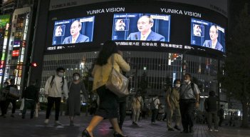 Peatones en calle ven una transmisión de televisión del primer ministro de Japón, Yoshihide Suga, anunciando el levantamiento del estado de emergencia por coronavirus./ AFP 