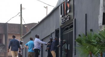 Transeúntes pasan junto a los policías que hacen guardia en la entrada del club nocturno Livs, donde se produjo un incendio mortal en el distrito de Bastos de Yaundé. / Foto: AFP